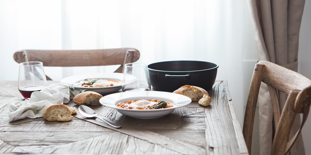 Gedeckter Tisch mit zwei Tellern, Brot und Rotweingläsern